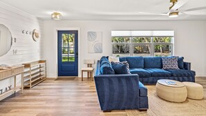 Un salon moderne avec un canapé bleu, des étagères en bois et une grande fenêtre donnant sur un paysage verdoyant.