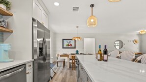 Une cuisine moderne dotée d’un réfrigérateur en acier inoxydable, d’un plancher en bois, d’un comptoir en marbre et de luminaires suspendus.