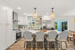 A modern kitchen with white cabinets, a stainless steel refrigerator, and a central island with bar stools.