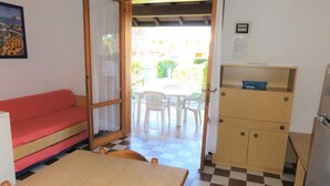 A room with a checkered floor, a wooden table, a red sofa, a wooden cabinet, and a door leading to an outdoor area with a table and chairs. - Lovely Two-storey Flat (San Michele al Tagliamento)