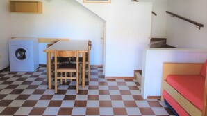 A compact room with a checkered floor, a washing machine, a small table with chairs, a bed, and a staircase. - Lovely Two-storey Flat (San Michele al Tagliamento)