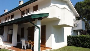Una casa blanca de dos pisos con techo verde, un porche cubierto con mesa y sillas, y una antena parabólica.