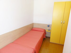 A small, single-bed room with a wooden headboard, a yellow wardrobe, and a bedside table with a lamp. - Lovely Two-storey Flat (San Michele al Tagliamento)