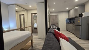 A modern hotel room with a bed, a sofa, a small dining table, and a kitchenette. - Pool Side Retreat- 1 BED TC-B105 (Sa Khu)