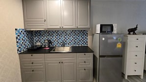 A compact kitchen with grey cabinets, a stainless steel refrigerator, a microwave, and a tiled backsplash. - Pool Side Retreat- 1 BED TC-B105 (Sa Khu)
