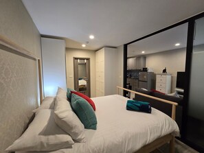 A modern bedroom with a large bed, a wooden headboard, and a sliding glass door leading to a kitchenette.
