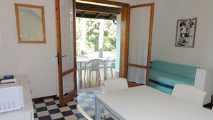 A room with a checkered floor, a white table, white chairs, a teal sofa, and a wooden-framed door leading outside. - Charming Two-storey Flat (San Michele al Tagliamento)