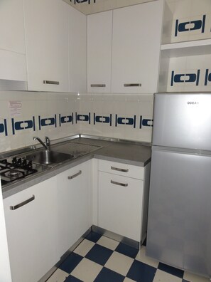 Een keuken met witte kastjes, een roestvrijstalen koelkast en een geruit vloertje.