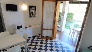 A room with a checkered floor, a white desk, a white chair, a microwave, a television, and a door leading to an outdoor area with a table and chairs. - Charming Two-storey Flat (San Michele al Tagliamento)