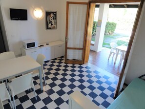 A room with a checkered floor, a white desk, a white chair, a microwave, a television, and a door leading to an outdoor area with a table and chairs. - Charming Two-storey Flat (San Michele al Tagliamento)