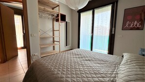 A bedroom with a large bed, a wooden wardrobe, and a sliding glass door to a balcony. - Bright Apartment Near the Beach (San Michele al Tagliamento)