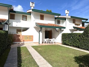 A white building with a tiled roof, a covered patio with outdoor seating, and a well-maintained lawn. - Nice Two-storey Flat (San Michele al Tagliamento)