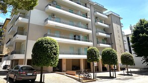 A multi-story residential building with balconies, a car parked in front, and neatly trimmed trees. - Cozy Apartment Close to the Beach (San Michele al Tagliamento)