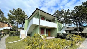 Ein zweistöckiges Gebäude mit Balkon, umgeben von Grün und Bäumen.