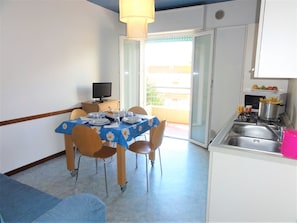 A compact kitchen with a dining area, a television, and a balcony with a view.