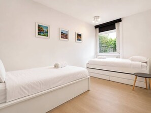 A minimalist bedroom with two beds, a small round table, and three framed pictures on the wall.