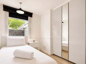 Een slaapkamer met een bed, nachtkastje met lamp, raam met gordijnen en een schuifdeurkast.