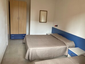 Een slaapkamer met twee bedden, een garderobe, een nachtkastje en een wandlamp.