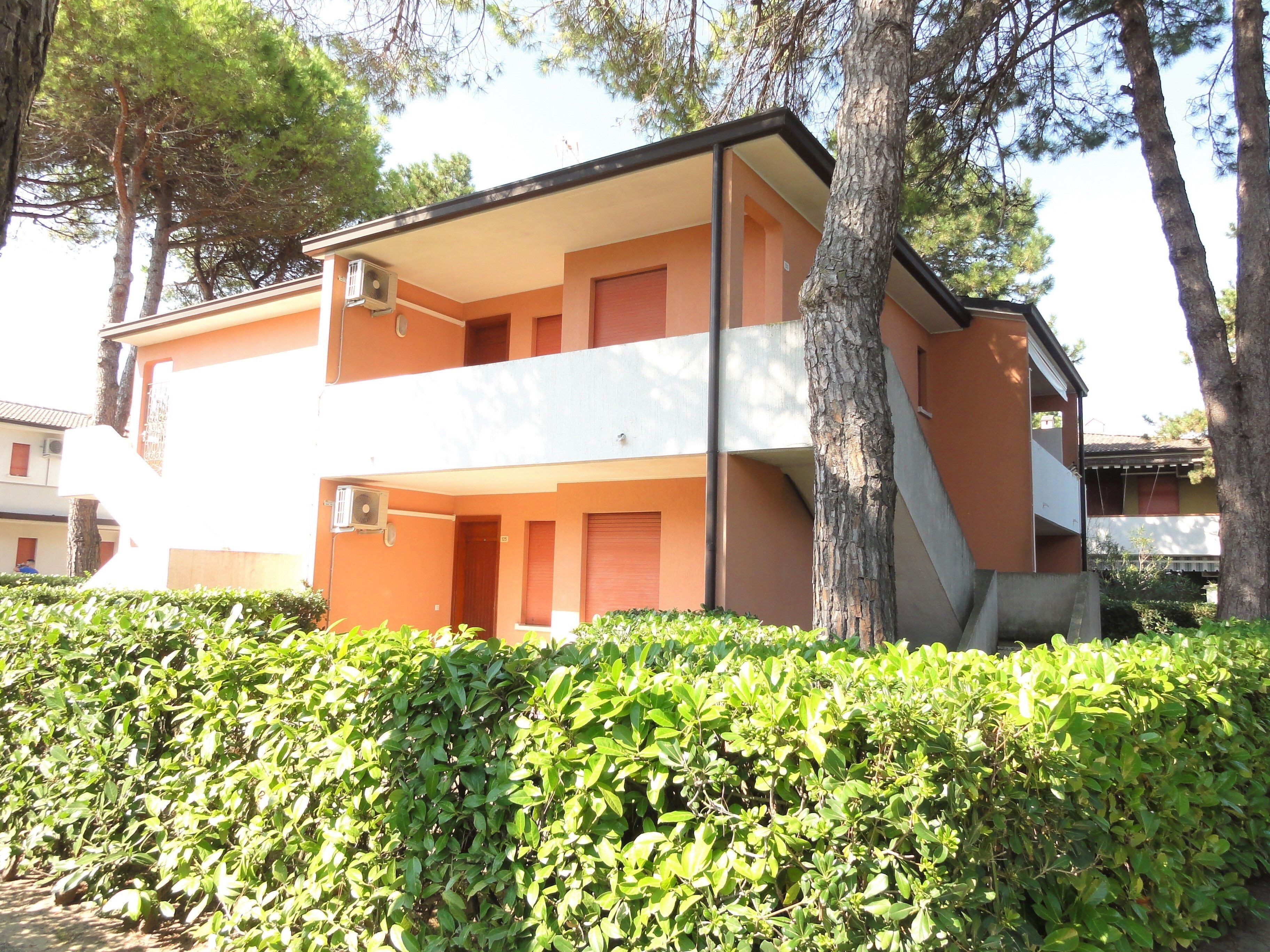 A two-story building with a flat roof, surrounded by greenery and trees.