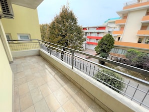 Ein Balkon mit Fliesenboden, Metallgeländer und Blick auf benachbarte Gebäude und Bäume.