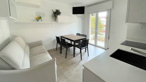 A modern kitchen with a dining area, a sofa, and a TV mounted on the wall. - Modern Apartment in Central Location (San Michele al Tagliamento)