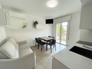 A modern kitchen with a dining area, a sofa, and a TV mounted on the wall.