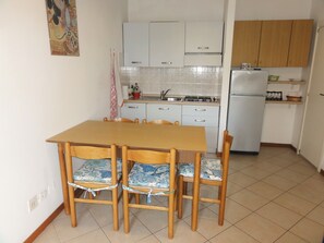 Cozinha compacta com armários brancos, uma mesa de madeira e quatro cadeiras com almofadas florais.