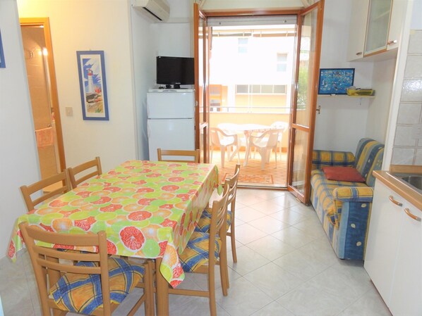 A compact kitchen with a dining area, a refrigerator, a television, and a sofa. - Apartment Near the Beach in Bibione (San Michele al Tagliamento)