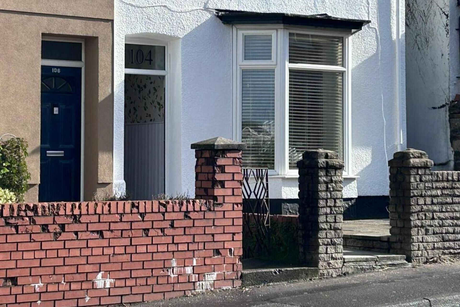A residential building with a blue door labeled '106', a white window with shutters, and a brick wall.