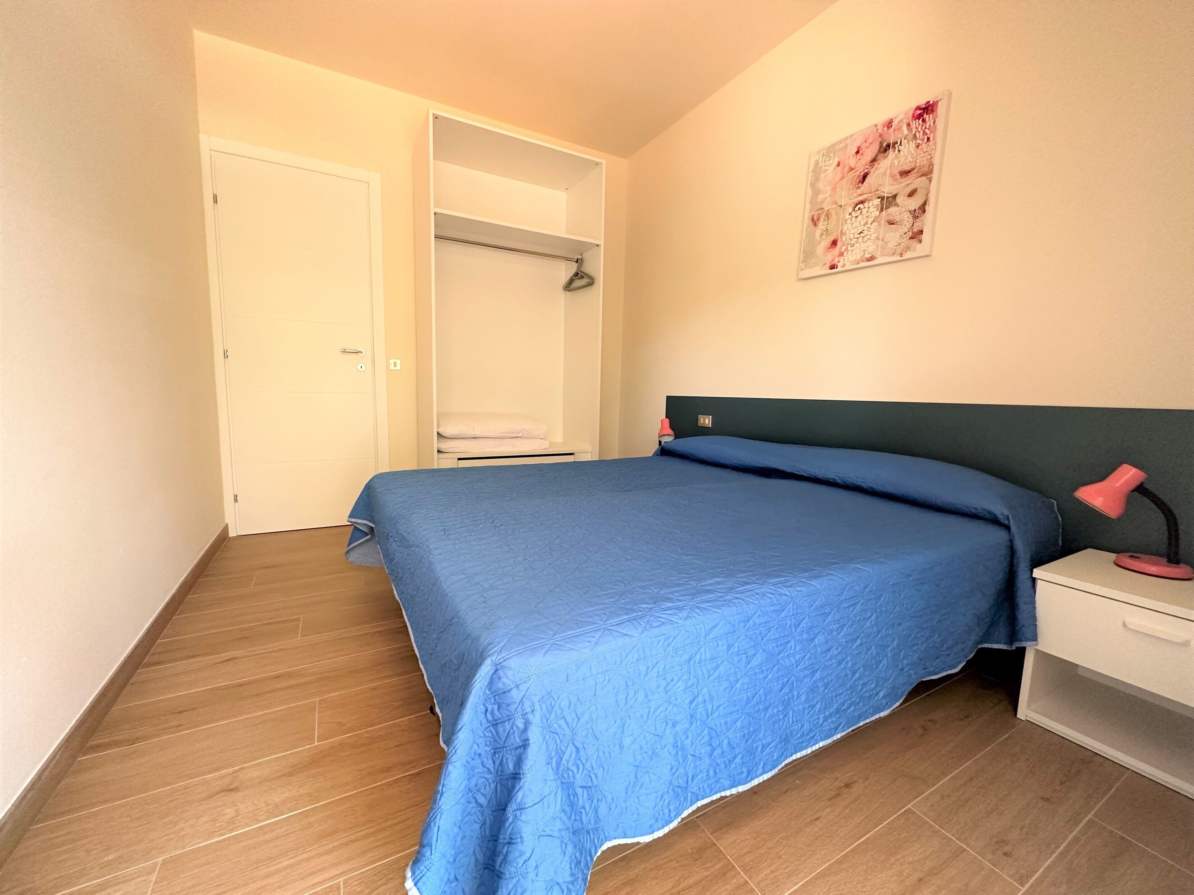 A bedroom with a bed, a nightstand, a wardrobe, and a wall-mounted artwork.
