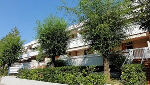 A residential building with multiple balconies, a white exterior, and surrounding greenery. - Apartment With Private Entrance in Bibione (San Michele al Tagliamento)