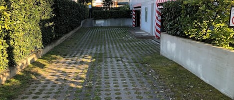 A paved pathway with circular patterns, bordered by hedges and a white building with red and white striped barriers.