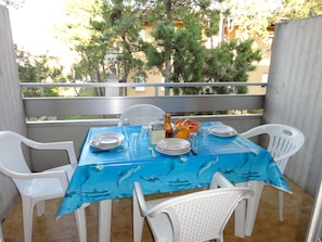 A balcony table set with plates, glasses, and a fruit basket, surrounded by white chairs. - Flat With Terrace Close to Beach (San Michele al Tagliamento)