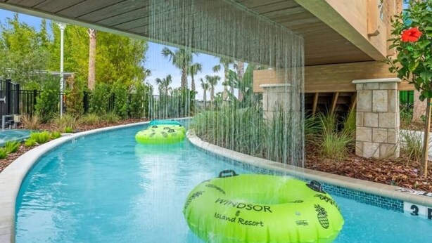 Una piscina con elementos acuáticos, incluyendo una cascada y anillos hinchables verdes con la leyenda 'Windsor Island Resort'.