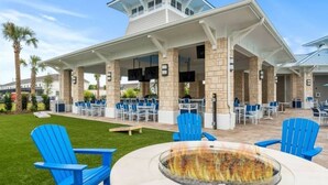 Un patio al aire libre con sillas Adirondack azules, un brasero y una zona de estar cubierta con mesas y sillas.