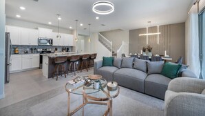 A modern kitchen with white cabinets, a central island with bar stools, and a dining area with a staircase. - Luxury 5BR Villa w/ Pool & Themed Rooms (DAVENPORT)