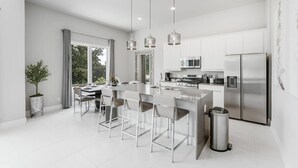 A modern kitchen with a central island, stainless steel appliances, and pendant lighting. - Modern 2-Story Loft w/ Pool Table – Near Disney (Kissimmee)