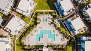 An aerial view of a modern residential area with a central swimming pool surrounded by lounge chairs and umbrellas, flanked by white buildings with blue accents. - Modern 2-Story Loft w/ Pool Table – Near Disney (Kissimmee)