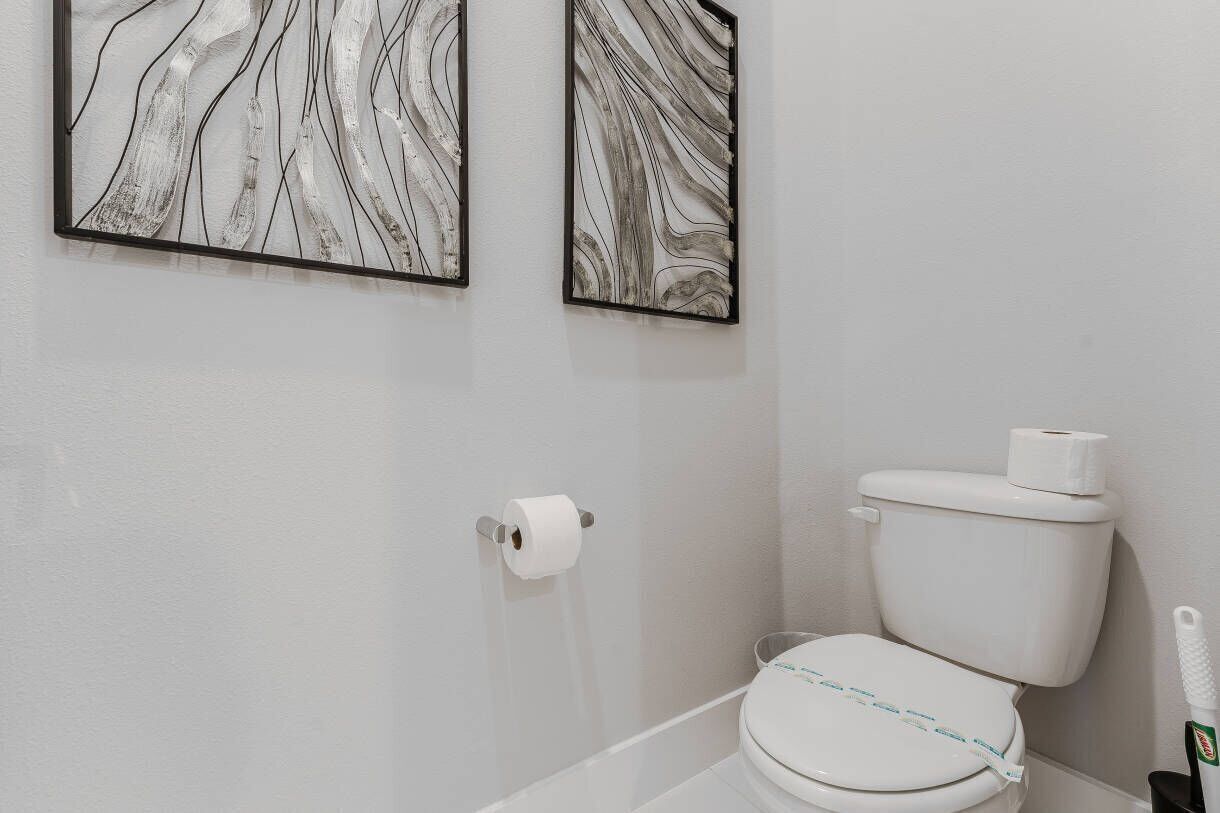 Une salle de bain avec des toilettes, un rouleau de papier toilette et deux œuvres d’art abstraites accrochées au mur.