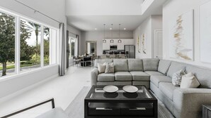 A modern living room with a grey sectional sofa, a black coffee table, and a dining area in the background. - Modern 2-Story Loft w/ Pool Table – Near Disney (Kissimmee)