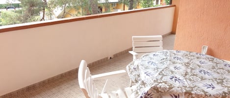 A balcony with a table and chairs, a patterned tablecloth, and a view of trees and buildings.