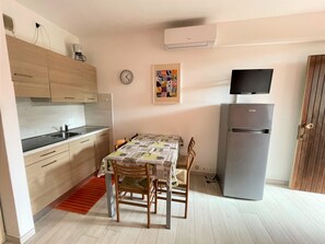 Een kleine keuken met een eettafel, stoelen, een koelkast, een klok en een flatscreen-tv.