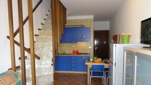 Une cuisine compacte avec des meubles bleus, un coin repas avec une chaise et un escalier menant à un autre niveau.