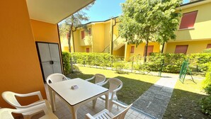 A patio with a table and four chairs, a tiled floor, and a view of yellow buildings and a garden. - Cozy Flat in a Villa With Shared Pool (San Michele al Tagliamento)