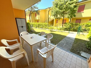 A patio with a table and four chairs, a tiled floor, and a view of yellow buildings and a garden. - Cozy Flat in a Villa With Shared Pool (San Michele al Tagliamento)