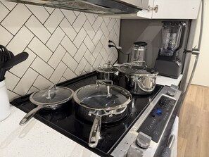 Uma cozinha com fogão preto, panelas de aço inoxidável, cafeteira e liquidificador.