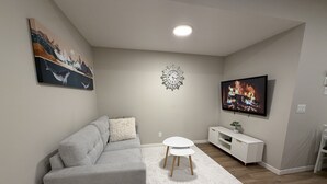 A living room with a grey sofa, a white rug, a TV, and a wall clock. - Cozy Basement Suite in Mahogany (Calgary)
