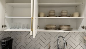 A kitchen with white cabinets, a herringbone tile backsplash, and a coffee maker on the counter. - Cozy Basement Suite in Mahogany (Calgary)