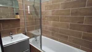 A modern bathroom with a glass-enclosed shower, a white sink, and a wooden vanity. - Le Bali Zen, studio with jacuzzi (Charavines)