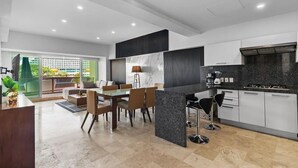 A modern kitchen with a dining area, featuring a marble backsplash, black granite countertop, and a large window overlooking a green outdoor area. - 4BR Marina Ocean-View Above Casino 2 Suites (Puerto Vallarta)